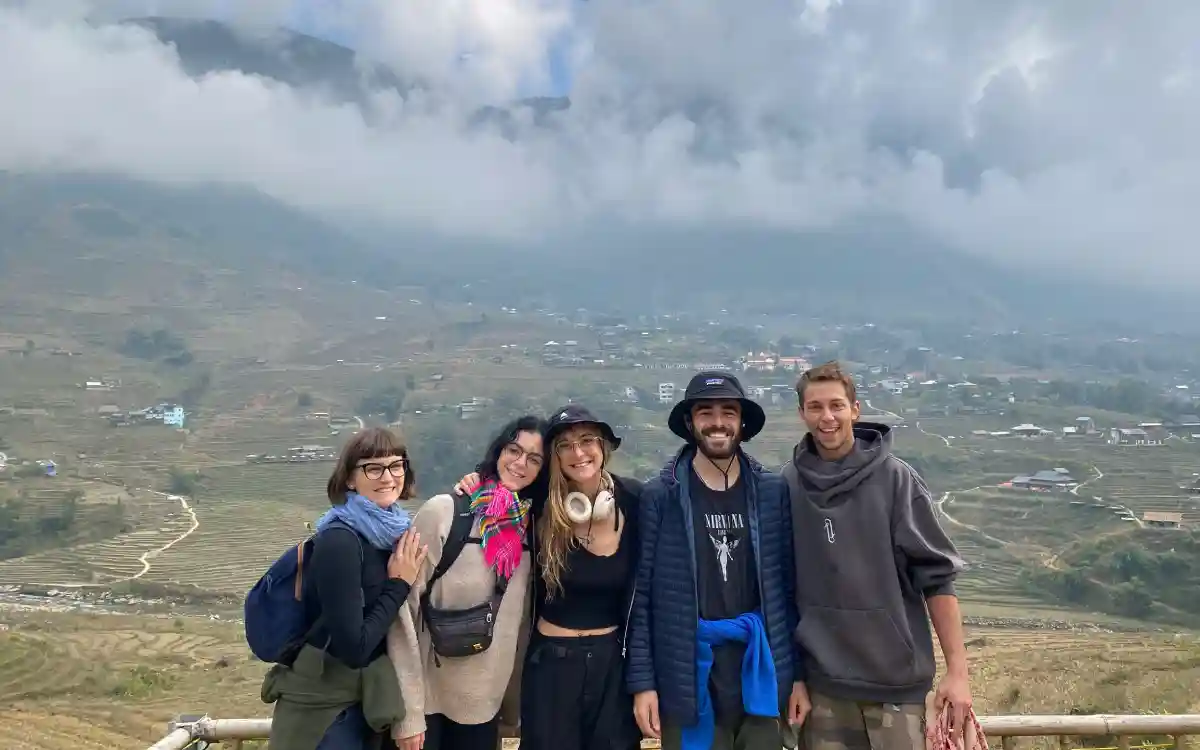 Small SapaTreks group smiling on a viewpoint above Muong Hoa Valley with clouds over the mountains