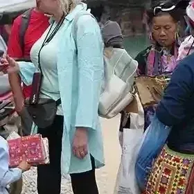 International travelers gathering with Hmong vendors and a small child on a street in a Sapa ethnic village before starting a walking tour