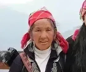 Young traveler standing between two Red Dao women elders in traditional indigo dress and red headscarves at a Sapa valley viewpoint