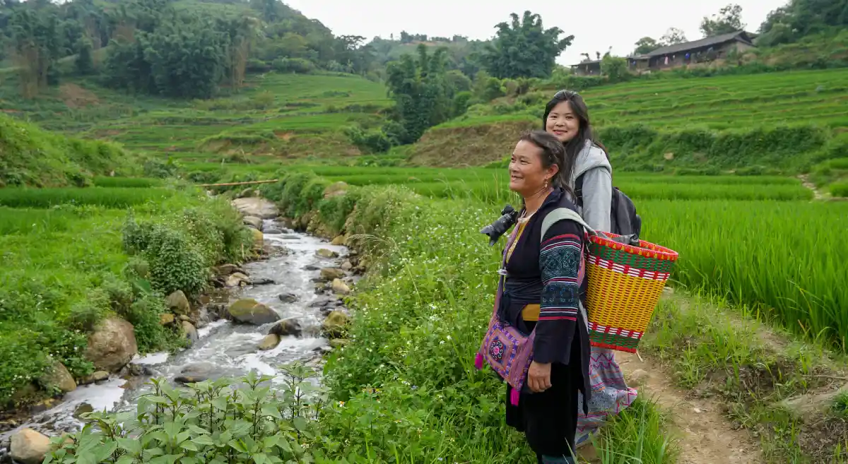 Hmong woman and young traveler walking along a stream beside lush rice terraces