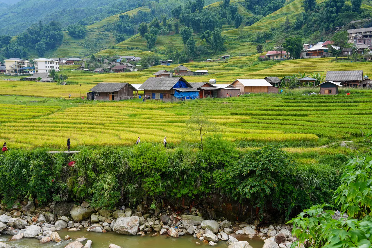 Wide green valley with stream, rice terraces and mountain village on the Classic Full-Day Valley Trek in Sa Pa