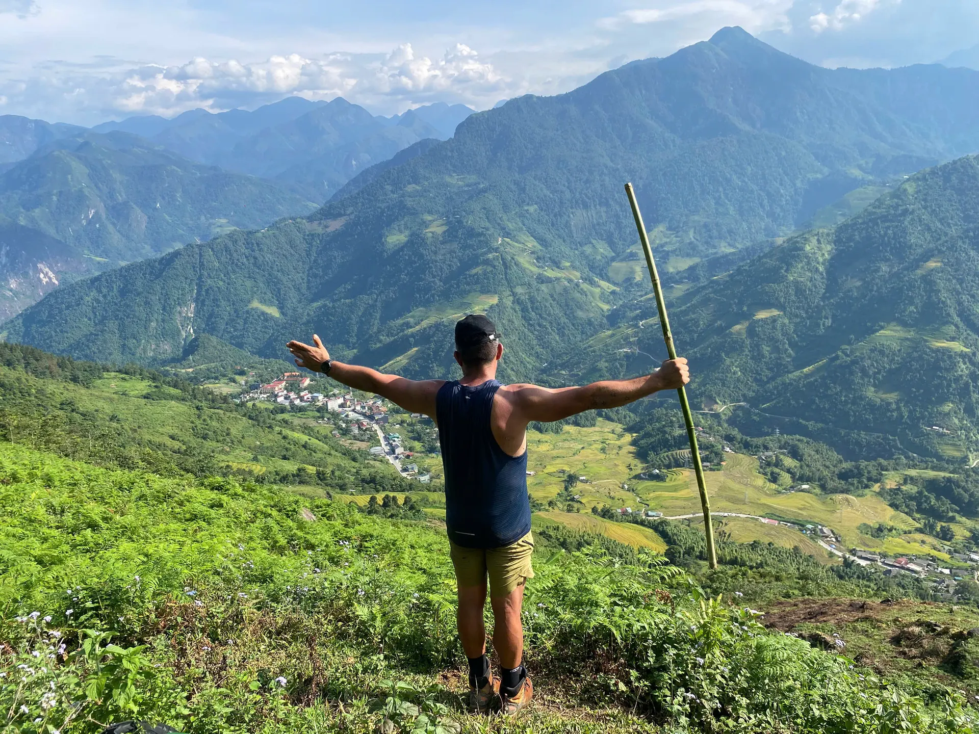 Trekker from behind on a ridge overlooking mountain valleys and rice terraces.