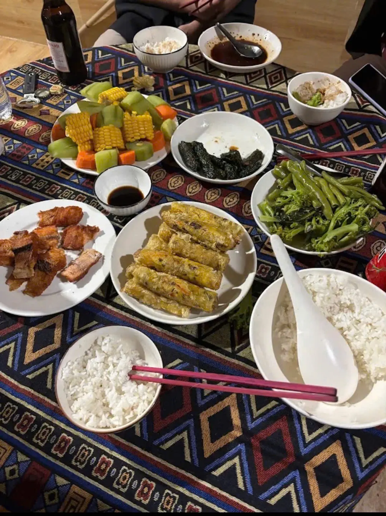 Shared meal of rice, vegetables, and fried dishes on a patterned tablecloth.