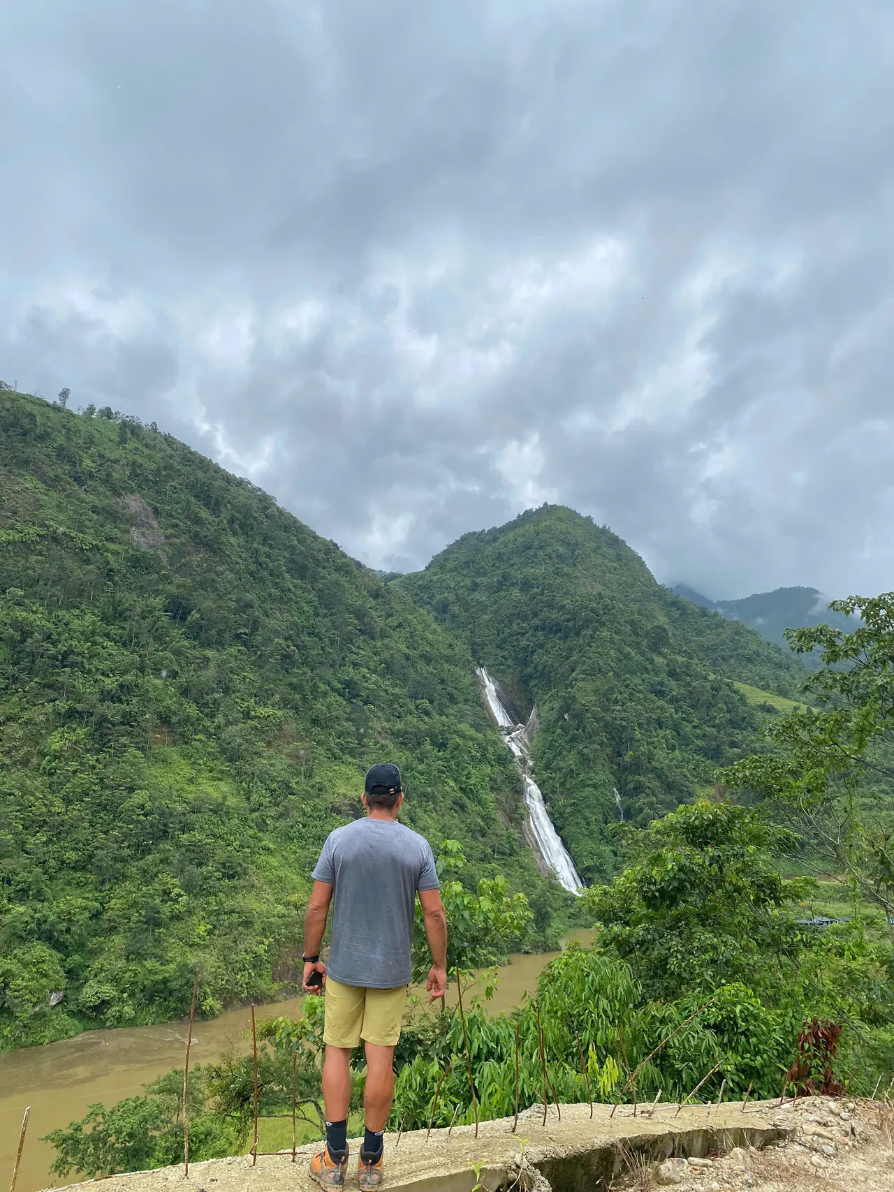 Hiker from behind looking toward a waterfall on a forested slope.